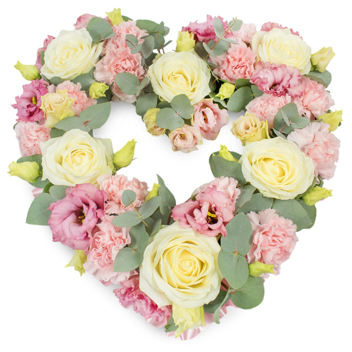 A meticulously crafted, heart-shaped funeral wreath is shown in full view, its outline perfectly defined by lush, pastel blooms that stand out crisply against a bright white background. The entire heart is densely covered in flowers, giving it a rich, luxurious look that still feels soft and comforting rather than overpowering. Creamy ivory and pale buttery-yellow roses form the main anchors of the design, spaced evenly around the heart so the eye is naturally drawn from one velvety bloom to the next. Each rose shows layers of tightly coiled petals at the centre, unfolding smoothly into rounded outer petals that suggest warmth and enduring affection. Nestled between the roses, blush and baby pink carnations add an intricate, ruffled texture, their frilled edges catching tiny shadows and creating a sense of depth and movement. Deeper rose-pink to mauve lisianthus, with their open, cup-like flowers and occasionally visible darker centres, are scattered artfully throughout, bringing a gentle contrast that gives the arrangement dimension without disturbing its pastel harmony. Interwoven among the flowers, silvery-green eucalyptus leaves arc gracefully, their rounded shapes and satin-matte finish forming a cool, calming border that traces the heart's curve. Small yellow-green buds peep through at intervals, suggesting freshness and the continuation of life. The mood is one of quiet grace, ideal for a tribute travelling from a family home in Enfield Wash to a service at a local church or crematorium. This heart-shaped wreath offers a touching way to say goodbye, expressing sympathy, remembrance, and deep love through expert floristry and a soft, peaceful palette.