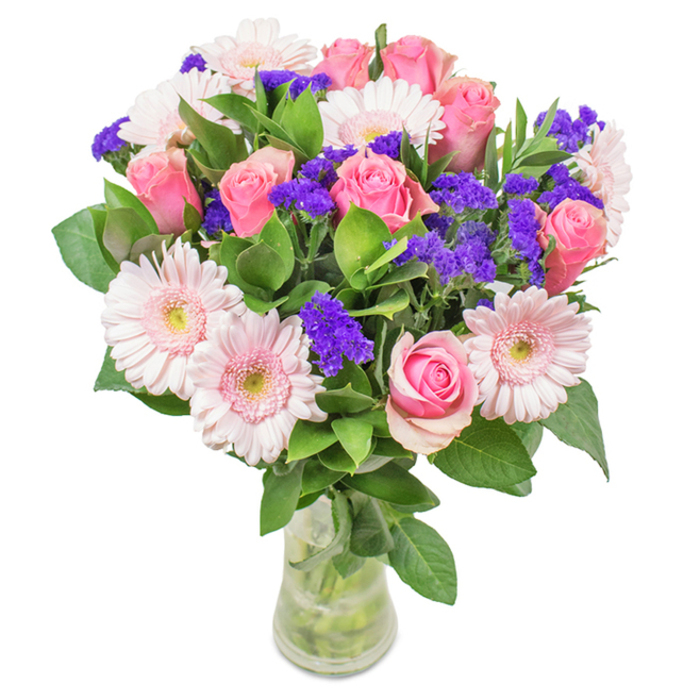 An exuberant, elegantly arranged bouquet set within a slender clear glass vase, proudly crafted by Enfield Wash florists and illuminated against a crisp white backdrop. The display features a central gathering of approximately 7-9 roses, their pink petals at various stages-from tightly formed buds to softly spiraling blooms-each catching the light with delicate charm. Intermixed are 5-7 pale pink gerbera daisies, their wide, friendly faces and finely detailed petals glowing with a subtle warmth reminiscent of late afternoons near Enfield Playing Fields. Throughout the arrangement, vivid purple statice or limonium create striking visual contrast and tactile diversity, infusing the bouquet with both vibrancy and a hint of wild garden spontaneity. Lush, deep green foliage encircles the base, suggesting local greenery and infusing the air with a refreshing, tranquil scent. The clear vase allows a view of the stems and glistening water, evoking the freshness and authenticity found in Enfield Wash's independent flower shops. Crafted for joyful occasions-from milestone birthdays and anniversaries to heartfelt gestures of affection-this arrangement, rich in local character, symbolizes celebration and thoughtful connection in the spirit of Enfield Wash.